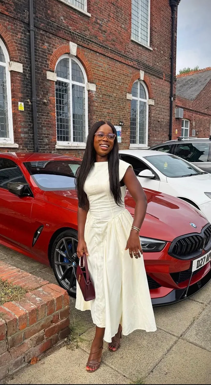 Precious smiling in an ivory dress beside a red car